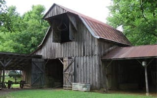A large, unpainted wooden barn with two awnings and antique farm equipment. This is Cooper Barn, which dates to the 1930s. 