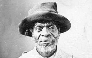 A black and white photo of an old Black man with a beard wearing a brown wide brimmed hat.