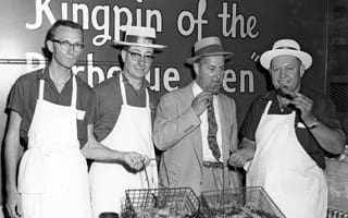 A black and white photo of four men standing behind a barbecue grill preparing for a barbecue contest. 