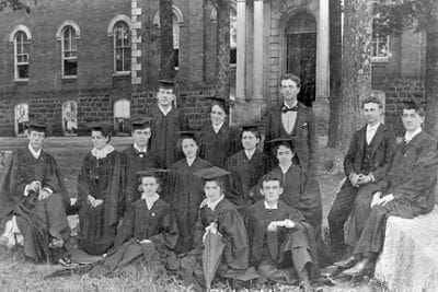 Black and white photo with 12 people in graduate gowns and mortar boards.