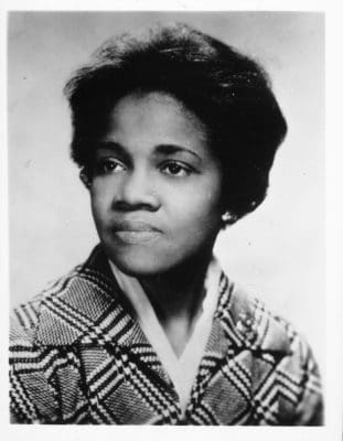 African-American woman with short dark hair, plaid jacket over a white blouse, looking to her right with a slight smile.
