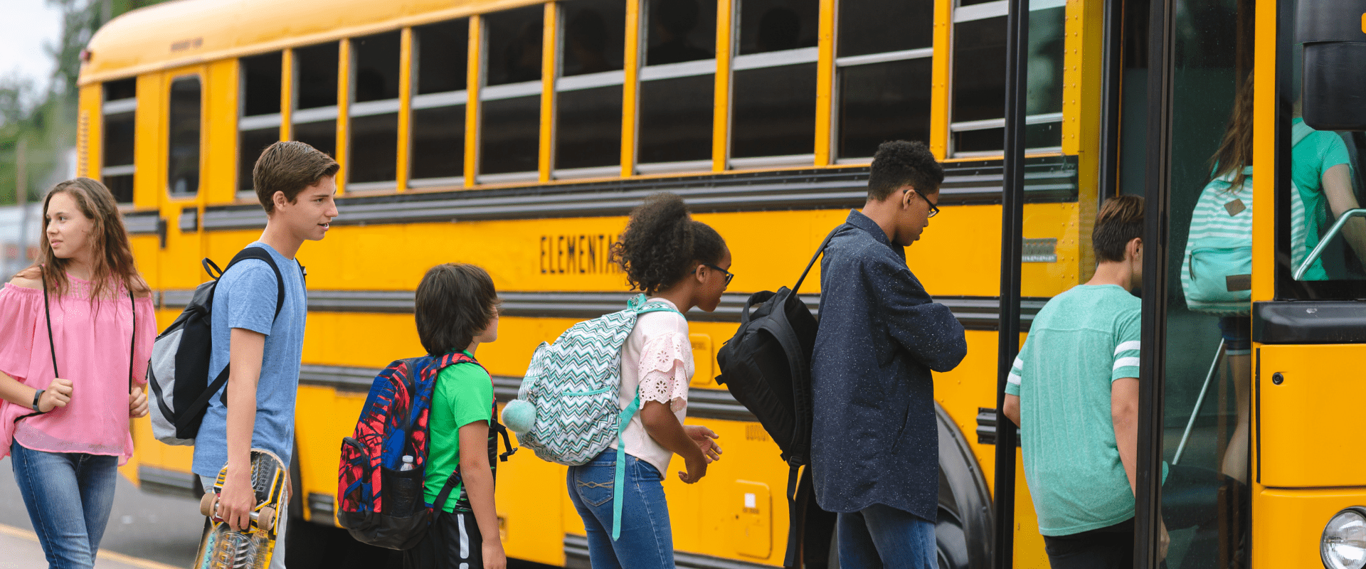 Yellow school bus with nine students of various heights and races in line to board the bus for a field trip.