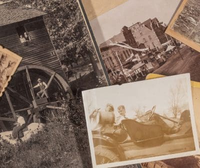 Partial view of sepia-toned photos stacked on each other that include part of a watermill, faded image of people and some buildings.