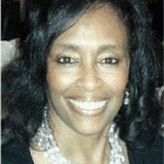 Portrait photo of a smiling woman with dark skin, black hair and white necklace.