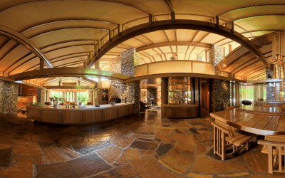 A warm, inviting interior with curved wooden beams, stone walls, and a spacious layout. The room features rustic furniture and large windows.