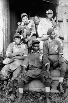 Historic black and white photo of a vintage baseball team. Six young men in uniforms and caps sit on steps, holding bats and gloves, conveying camaraderie.
